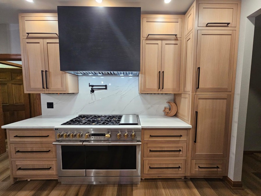 Natural oak shaker kitchen with a black wood range hood, brass hardware, and a marble backsplash