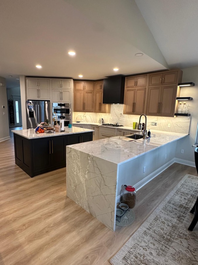 Open-concept kitchen with a black island, natural wood and cream perimeter cabinetry, black hood, and marble waterfall peninsula