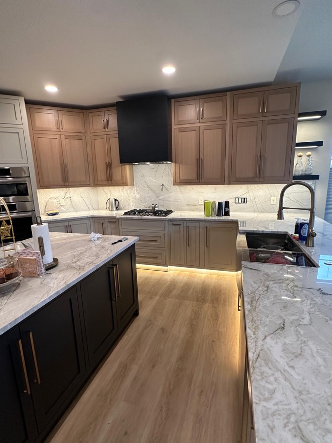 Kitchen with a gas cooktop under a black hood, cream cabinetry, dark island, and under-cabinet lighting