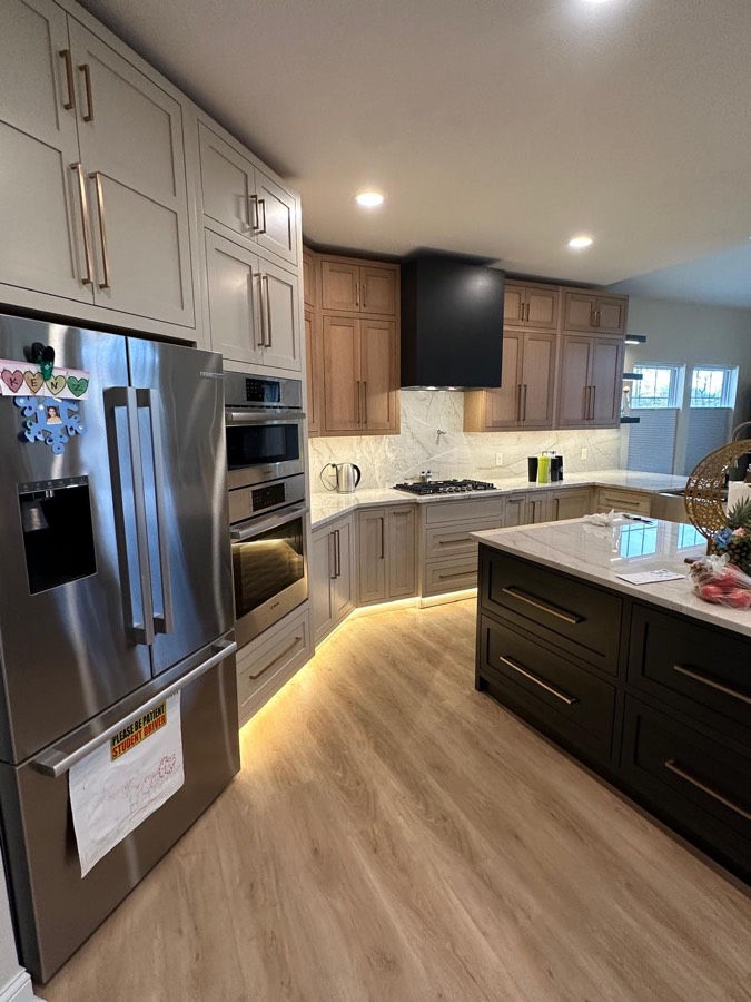 Kitchen with a stainless french-door refrigerator, stacked built-in ovens, and a dark island with a waterfall marble counter