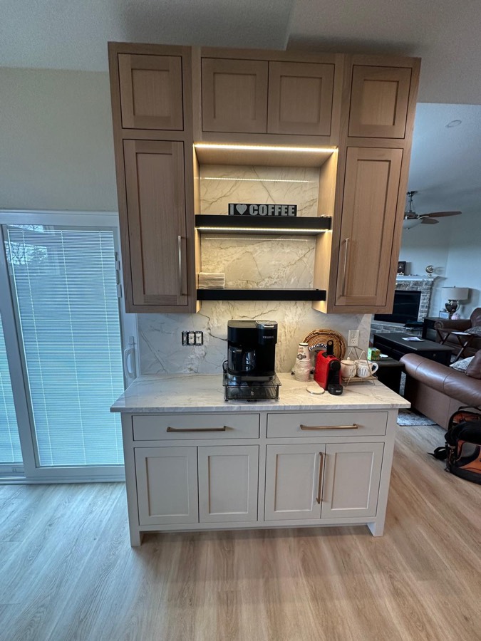 Custom two-tone coffee bar built-in with a backlit marble shelving niche and brass hardware