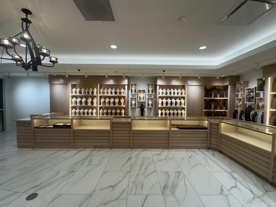 Oak jewelry showroom with glass display counters and backlit shelving under a chandelier