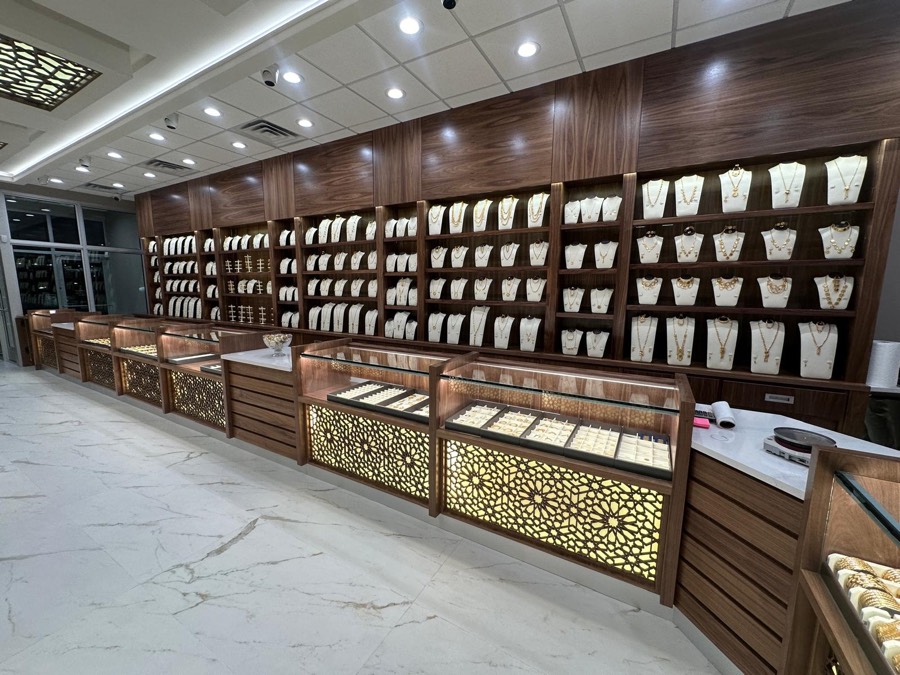 Commercial walnut millwork wall with backlit necklace shelving and patterned glass display cases in a jewelry store