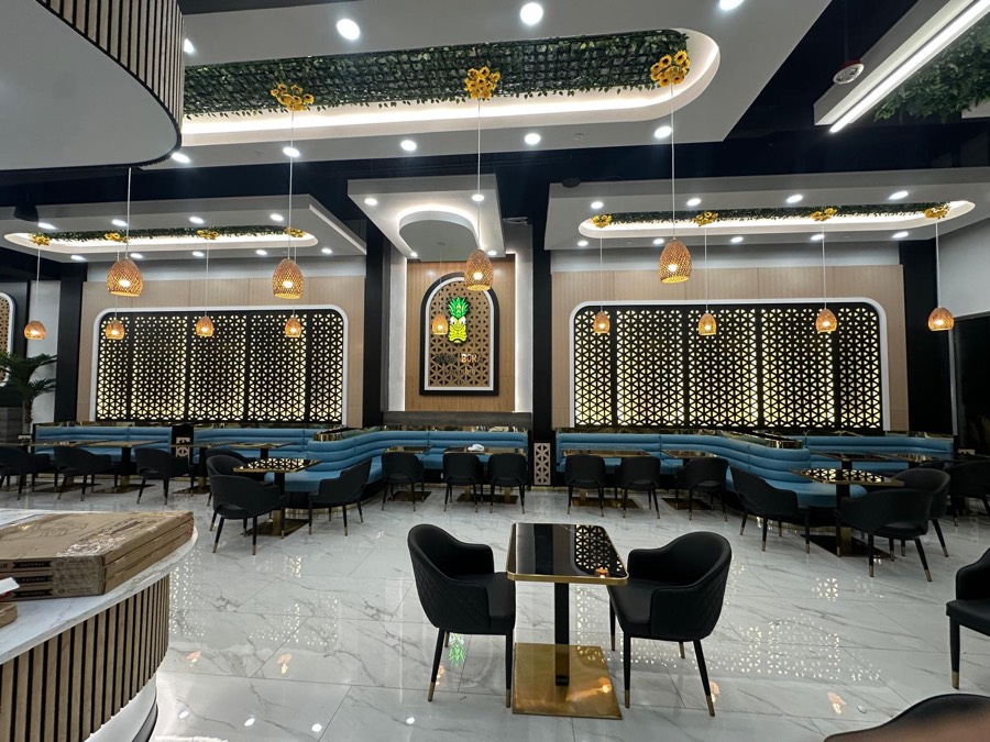 Tropical-themed café dining room with blue banquette seating, gold-trimmed tables, and backlit geometric wood screens