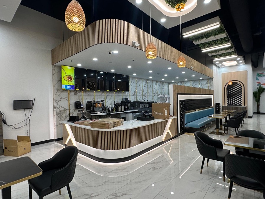 Curved wood-slat service bar with a marble countertop, espresso equipment, and rattan pendant lighting at a café